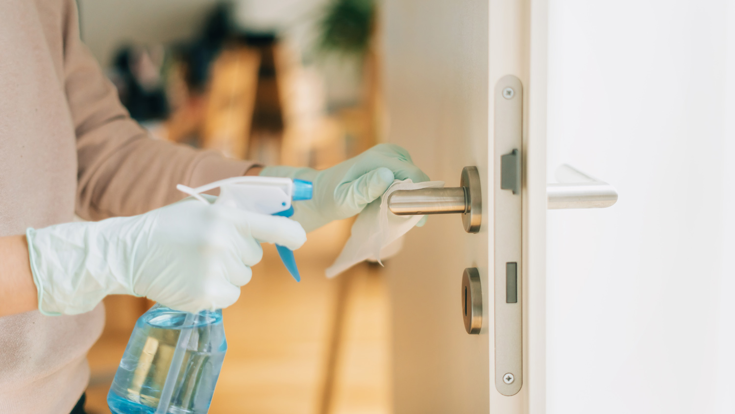 A woman cleaning a door handle with a disinfection spray