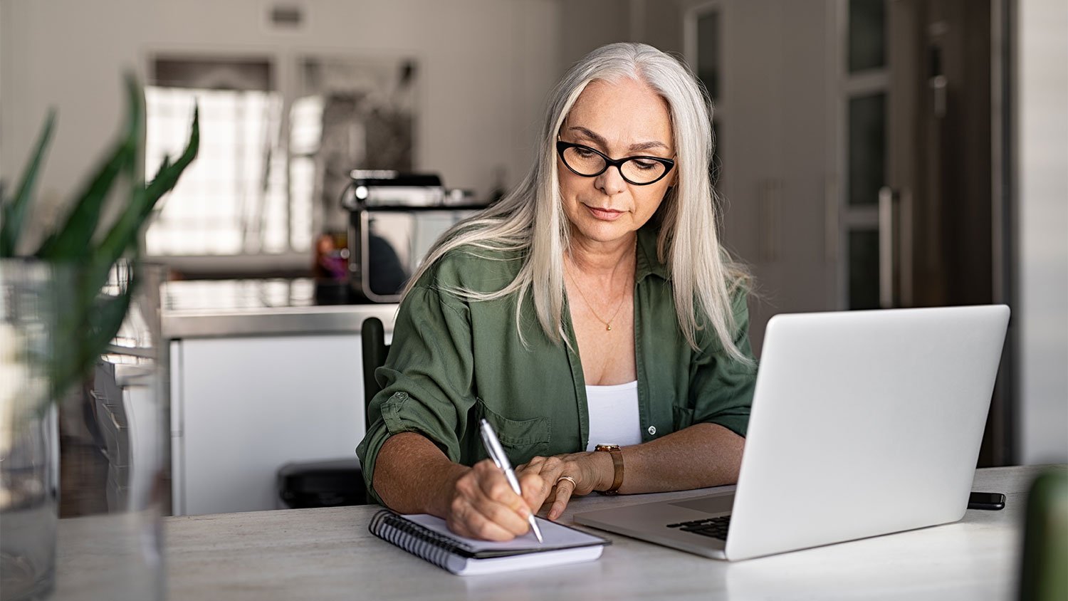 Woman using laptop and taking notes at home