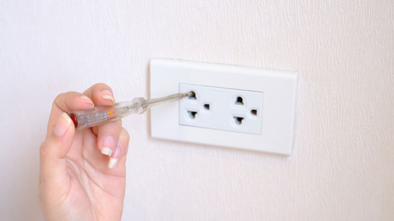 A woman using a tester screwdriver on an outlet