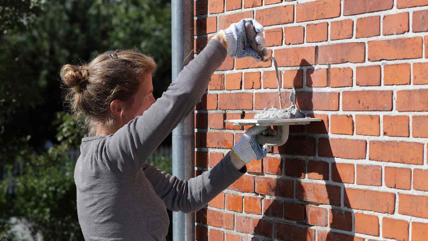 A woman tuckpointing a brick wall