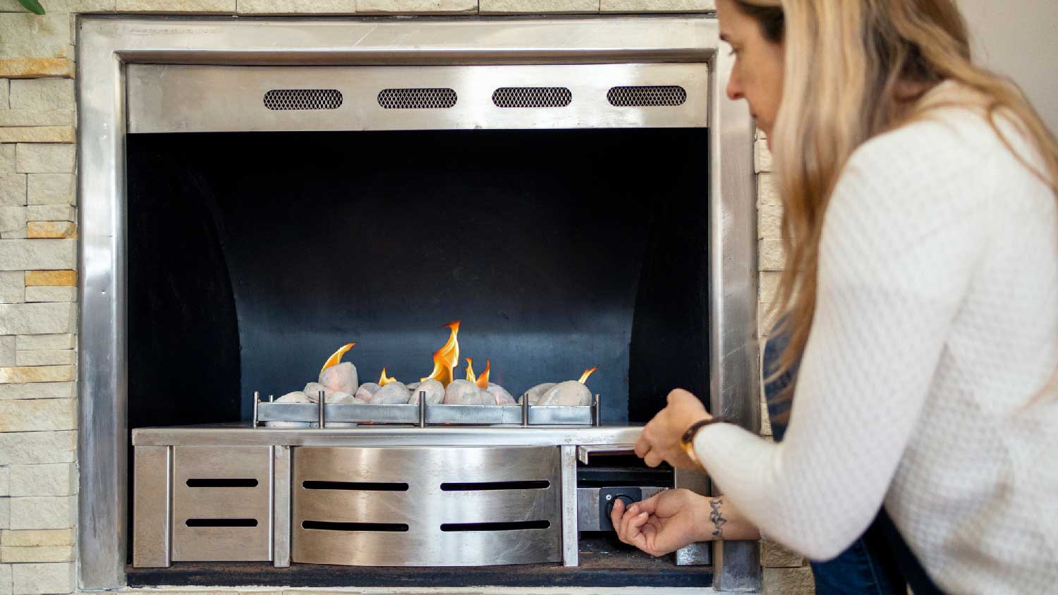 A woman turning on a gas fireplace