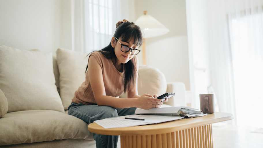 Woman checking notes and using her phone to do some calculations