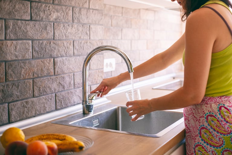 woman uses kitchen faucet to fill glass with water