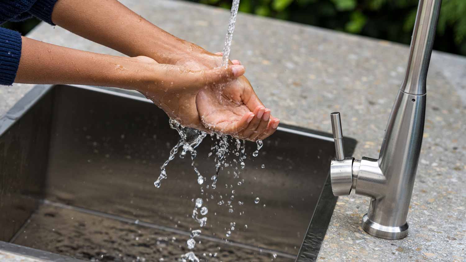 A woman washing her hands in an outdoor stainless steel sink 