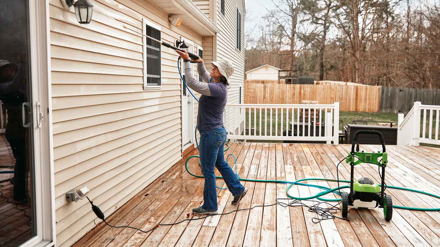 Woman using electric power washer to clean house siding