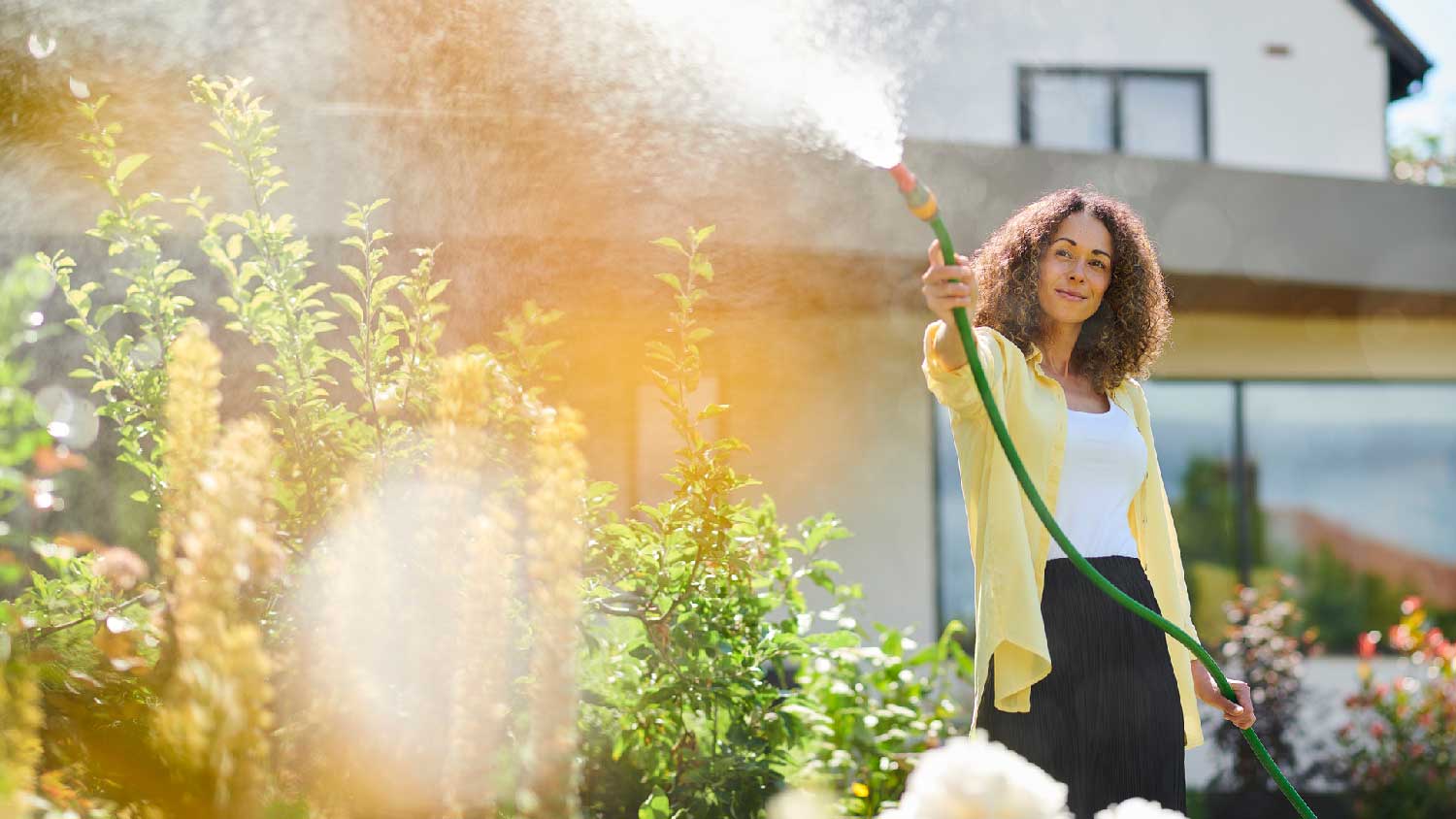 A woman watering bushes in her garden with the hose