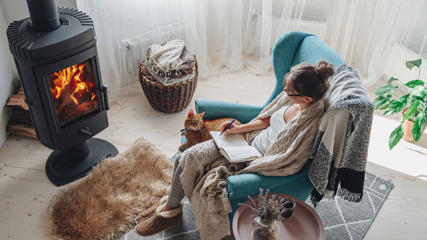 A woman writing on a notebook in front of a steel wood stove