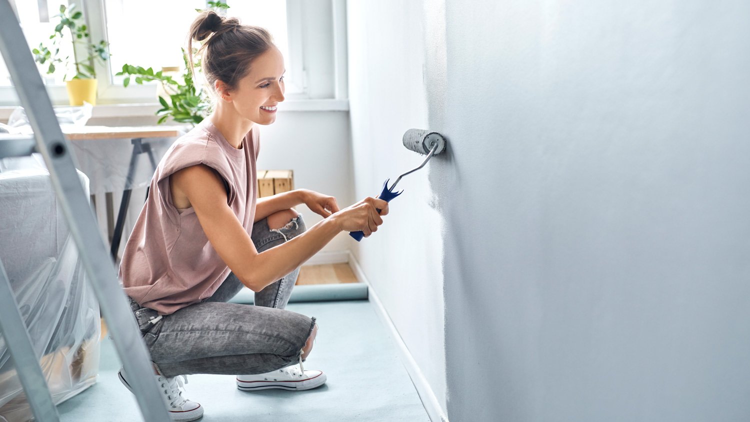 Young woman painting wall with paint roller while crouching at home