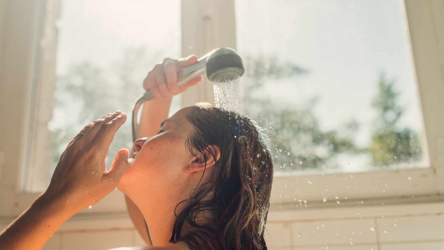 Woman washing hair with shampoo at a bright sunny day.