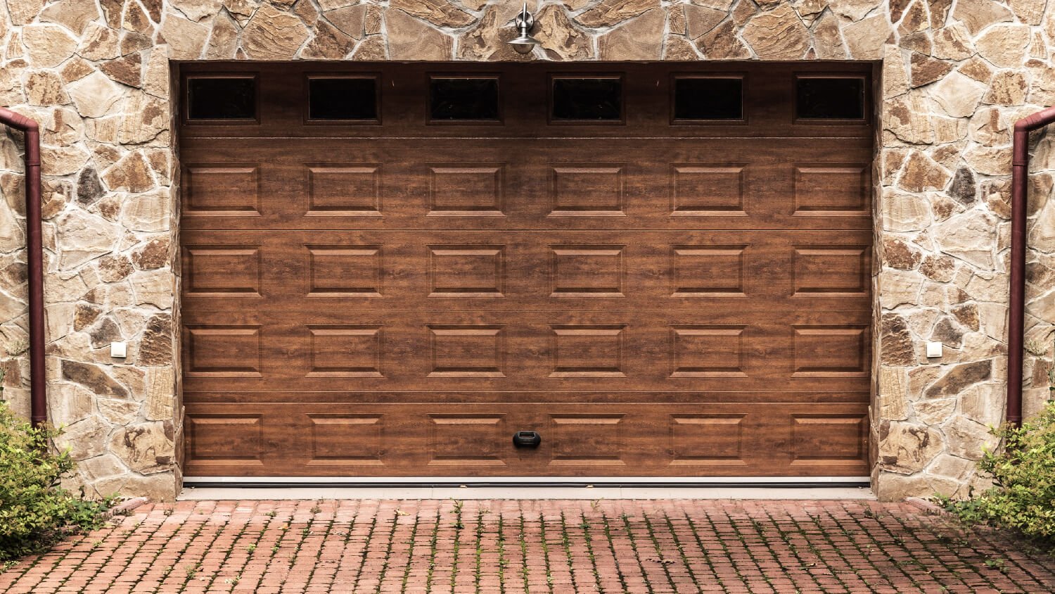 wood composite garage door with brick driveway and stone walls