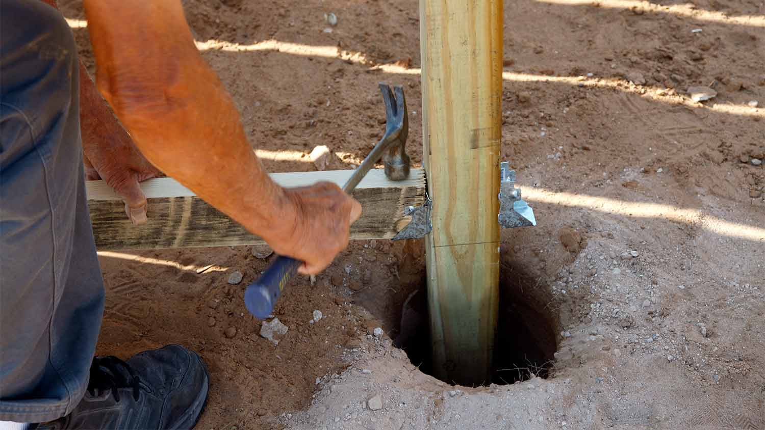 man building fence post with hammer