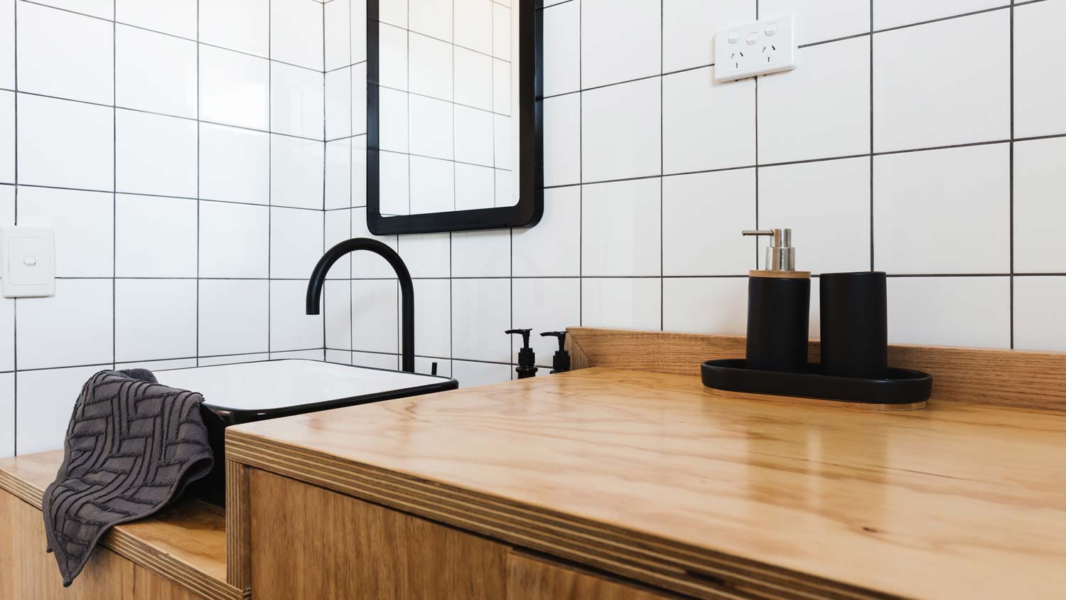 A wooden vanity and a black basin in a small bathroom