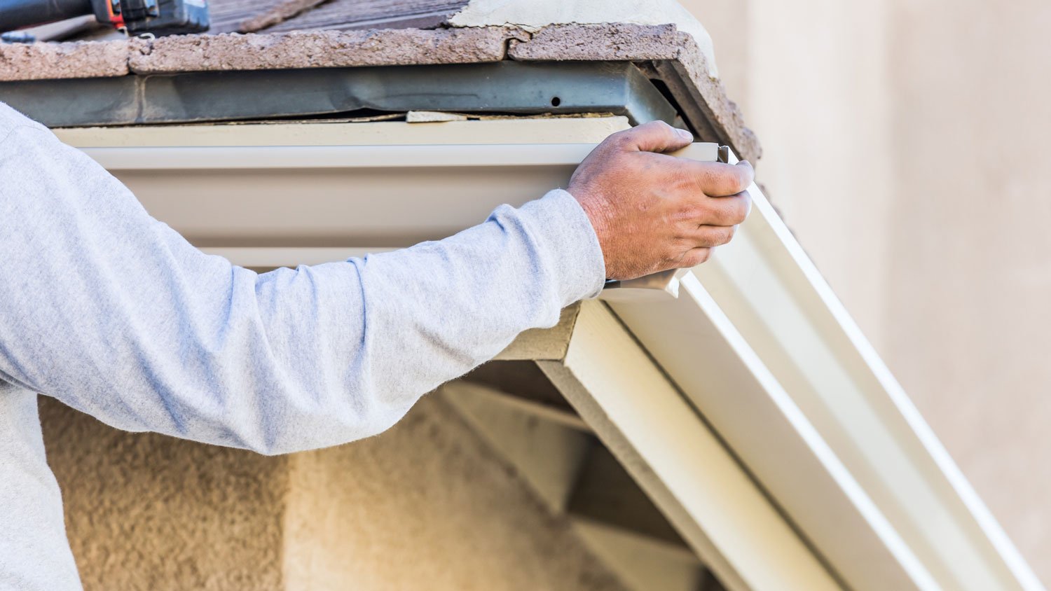 A worker adjusting a gutter in a house’s fascia