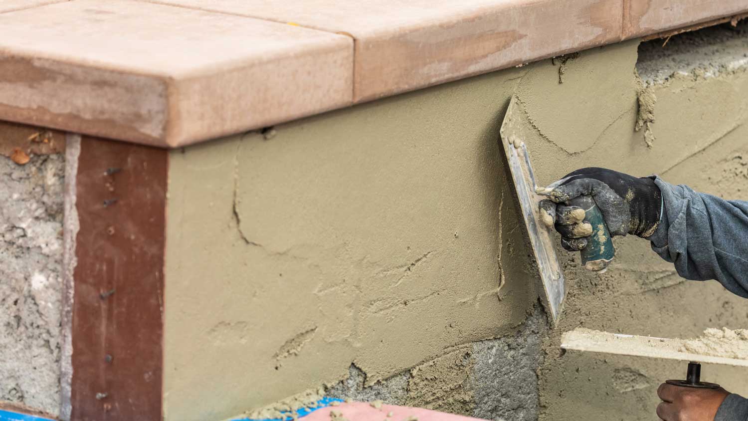 A worker applying stucco on a house’s refacing foundation