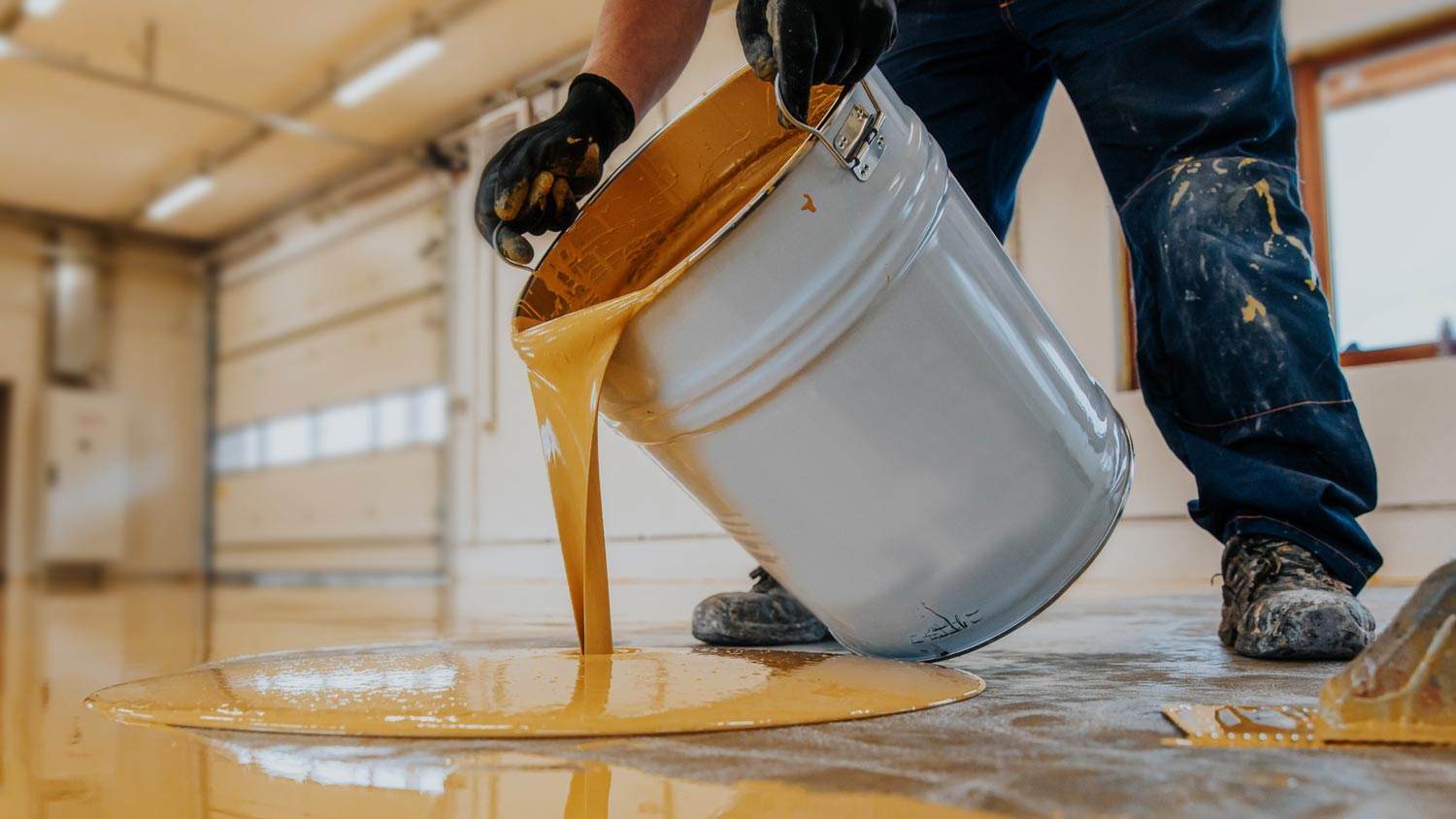 A worker applying yellow epoxy resin to a floor