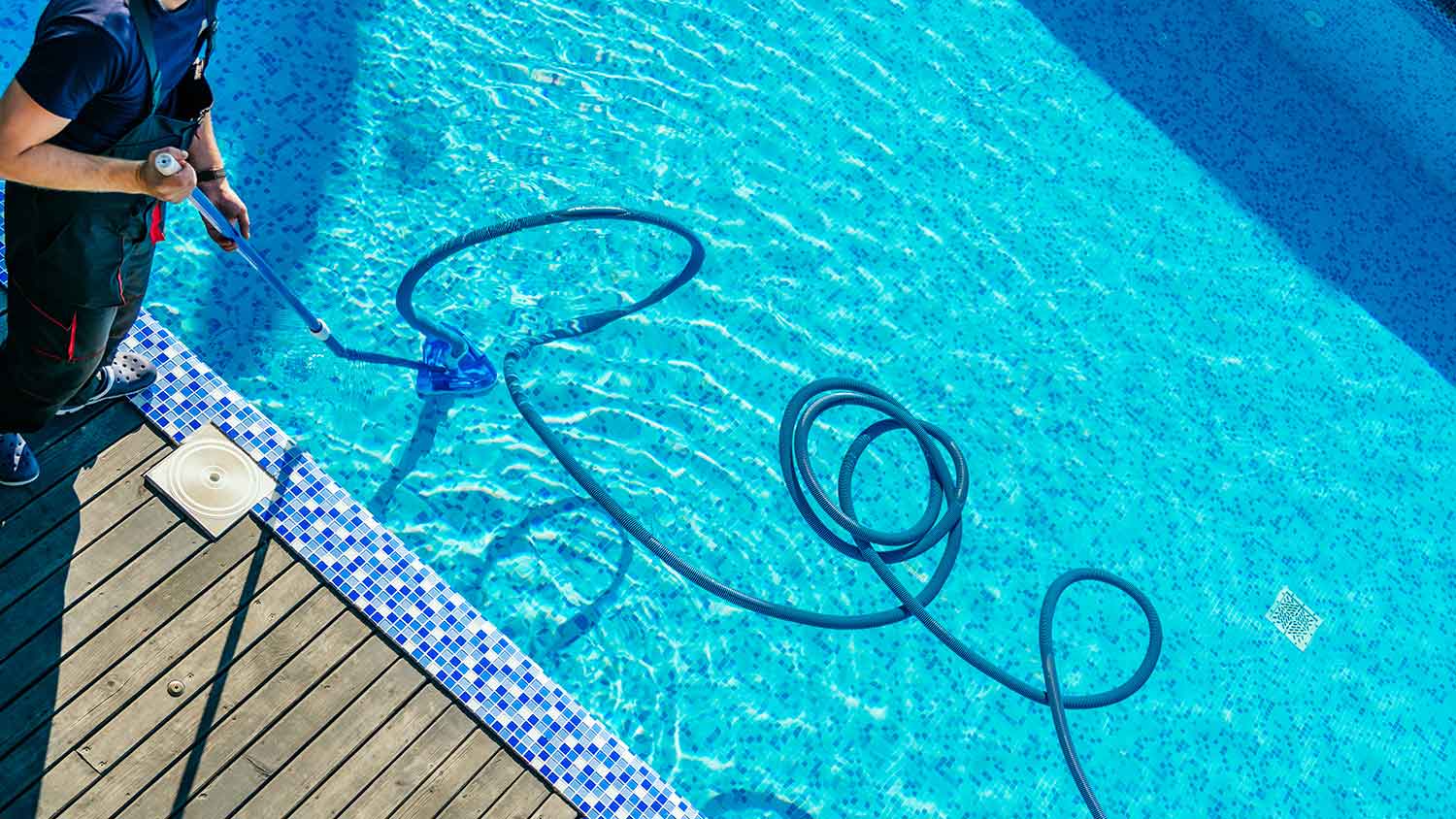 Worker using pool vacuum to clean the swimming pool