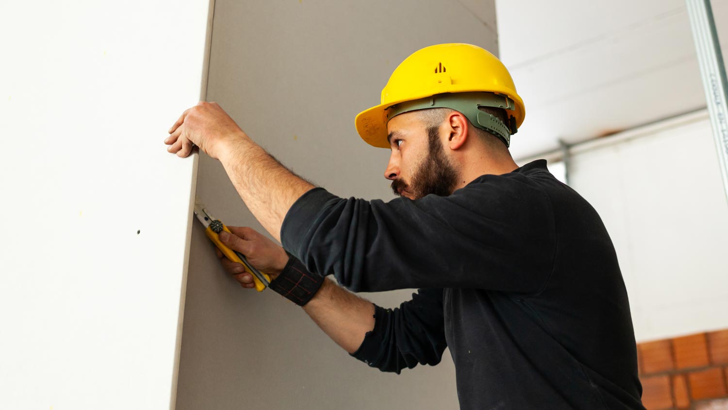 A worker cutting a drywall with a utility knife