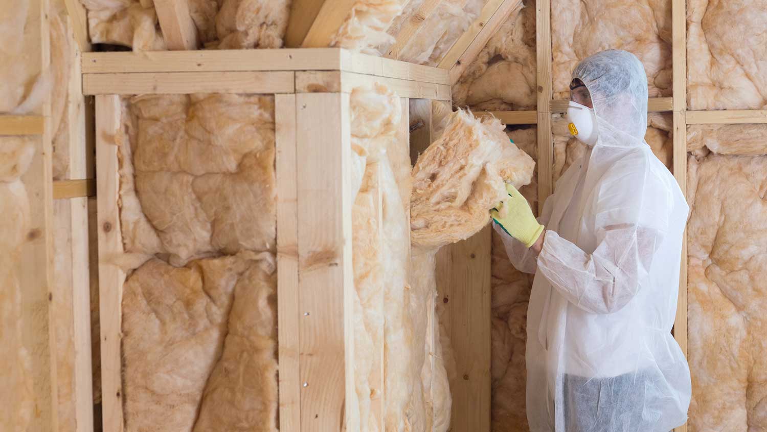 Worker installing fiberglass insulation in a wall framing