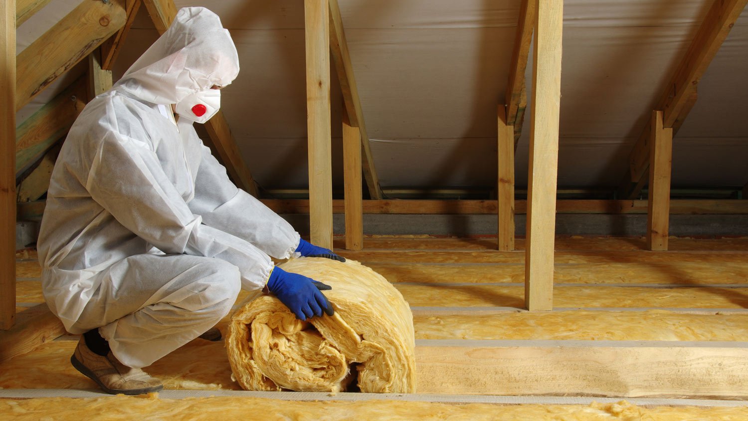 A worker in protective uniform insulating with wool a house’s atti