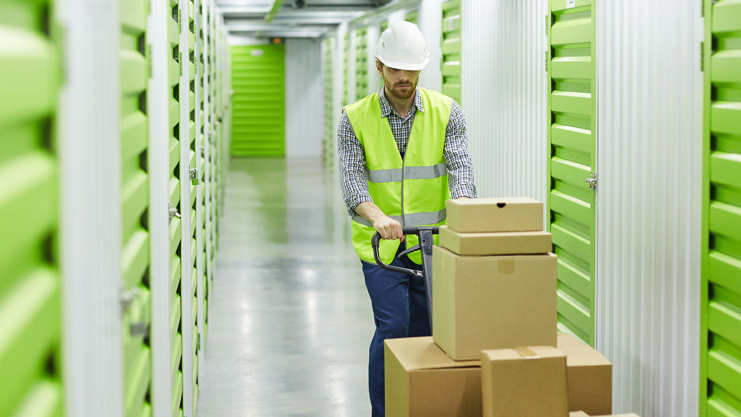 Worker in a self-storage unit pushing a cart with boxes