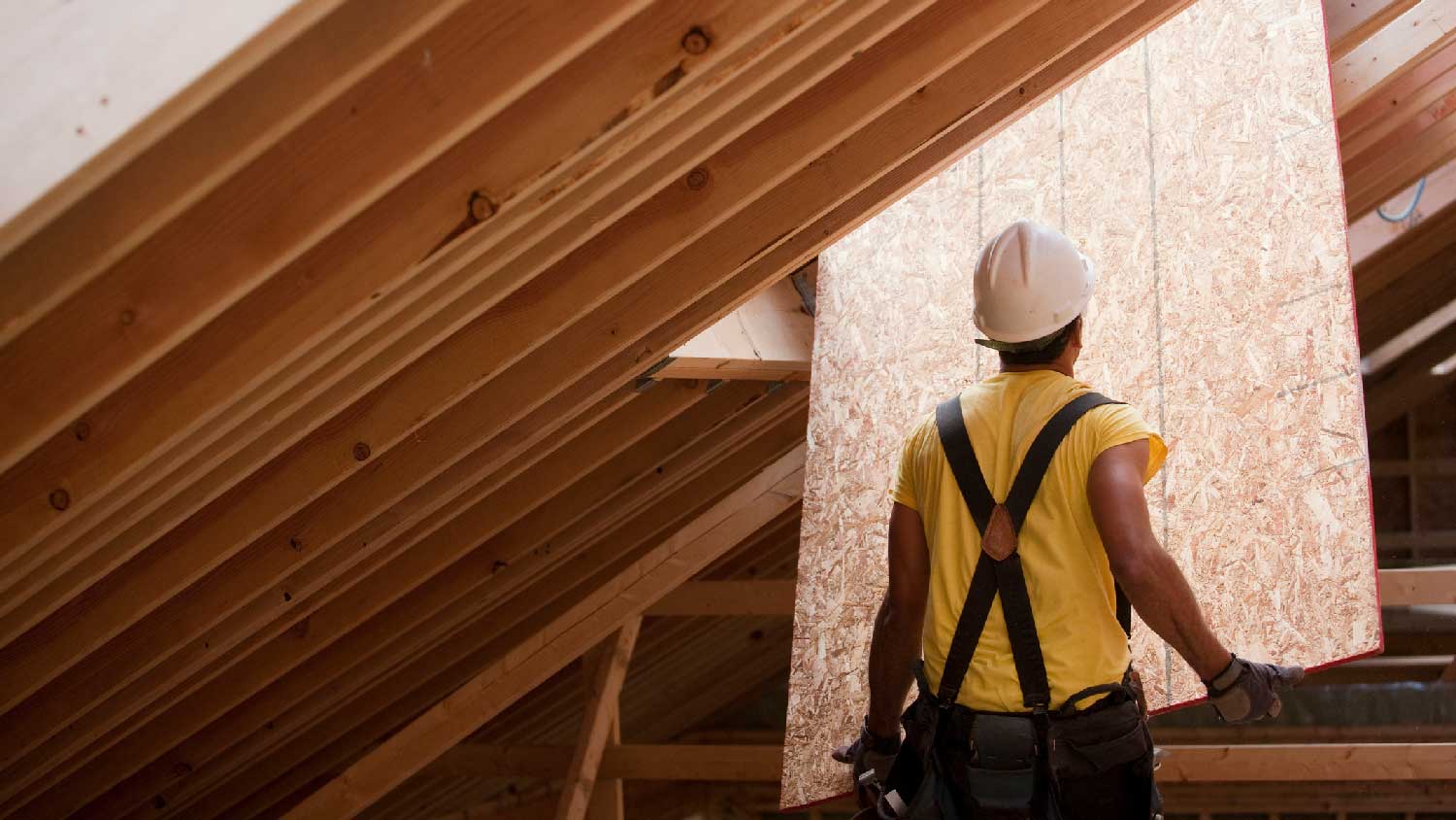 A worker pushing sheathing to the roof