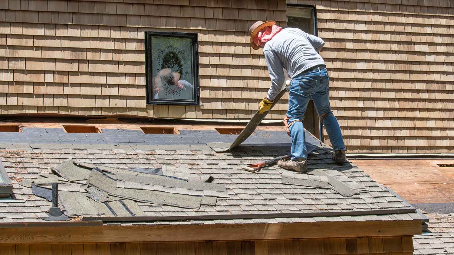 Worker removing old shingles from the roof of a house