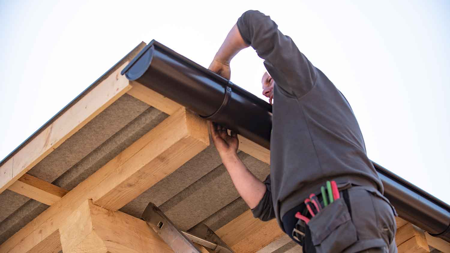 Worker on a ladder removing gutter from the roof