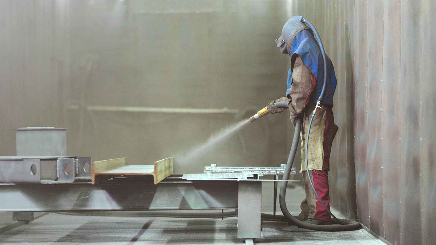 Worker wearing protective gear sandblasting metal