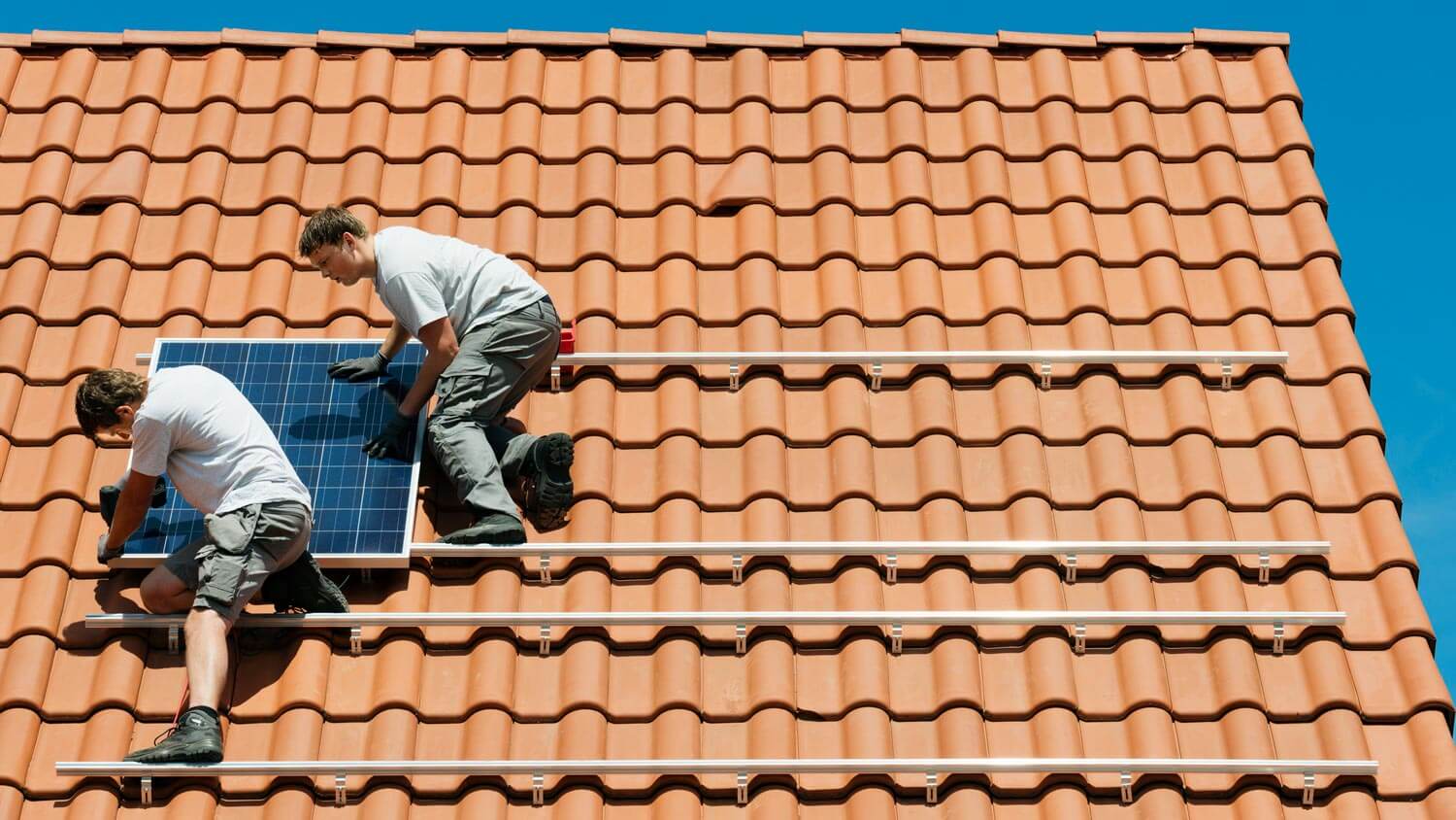 Workers installing new solar panels on roof framework of a house