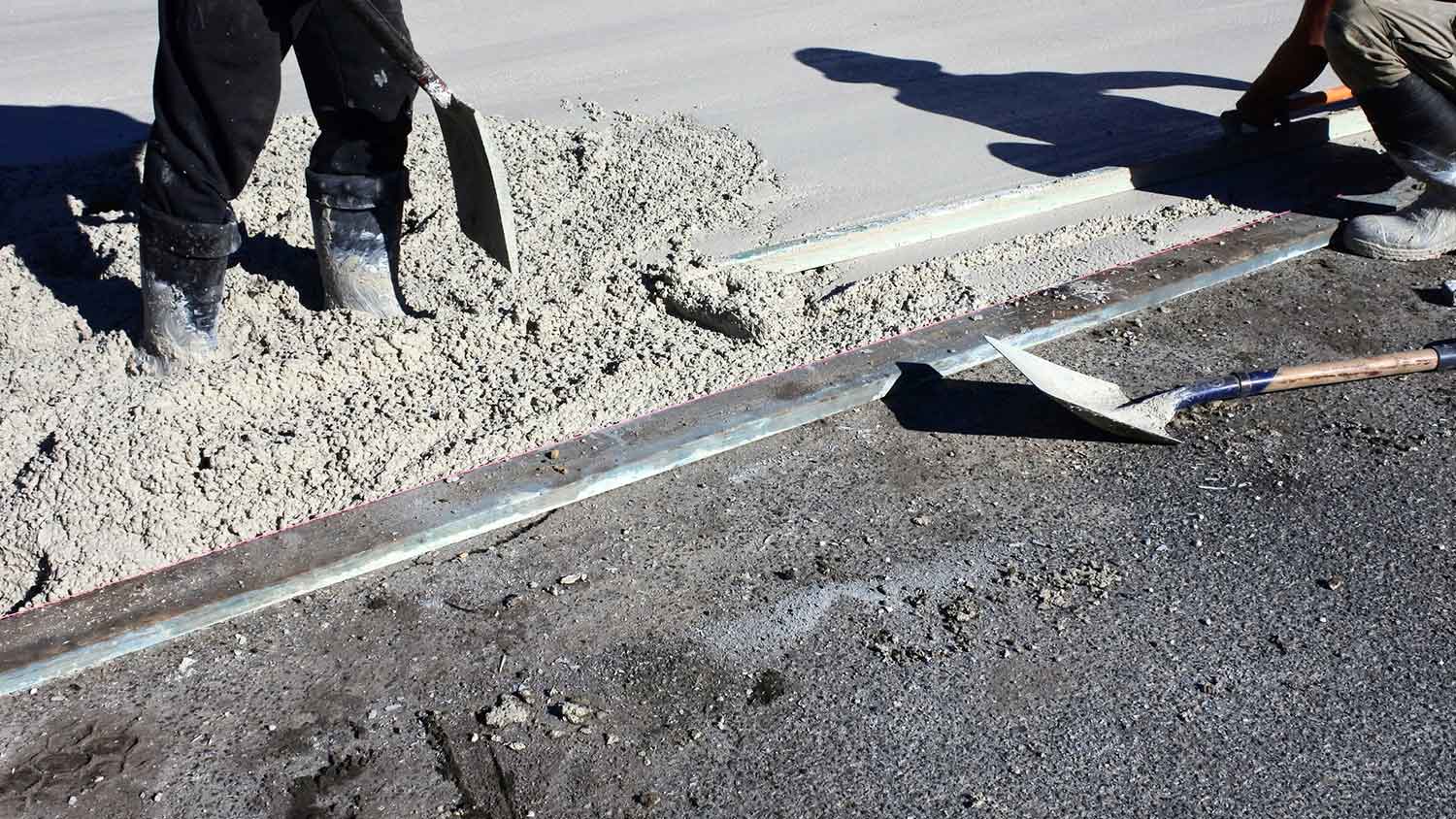 Workers pouring concrete over asphalt