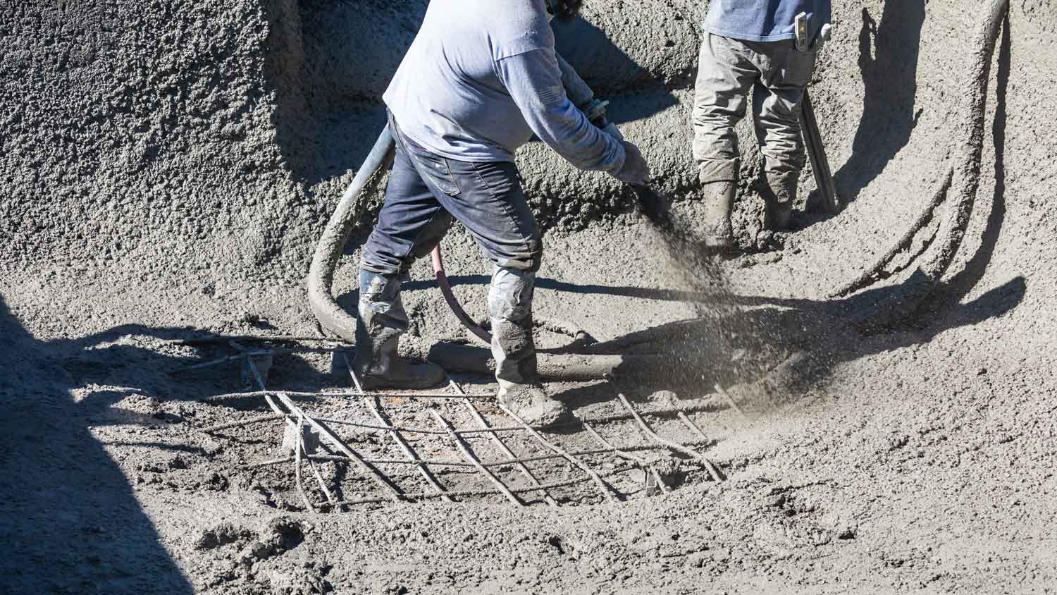 Two workers shooting concrete to build a gunite pool