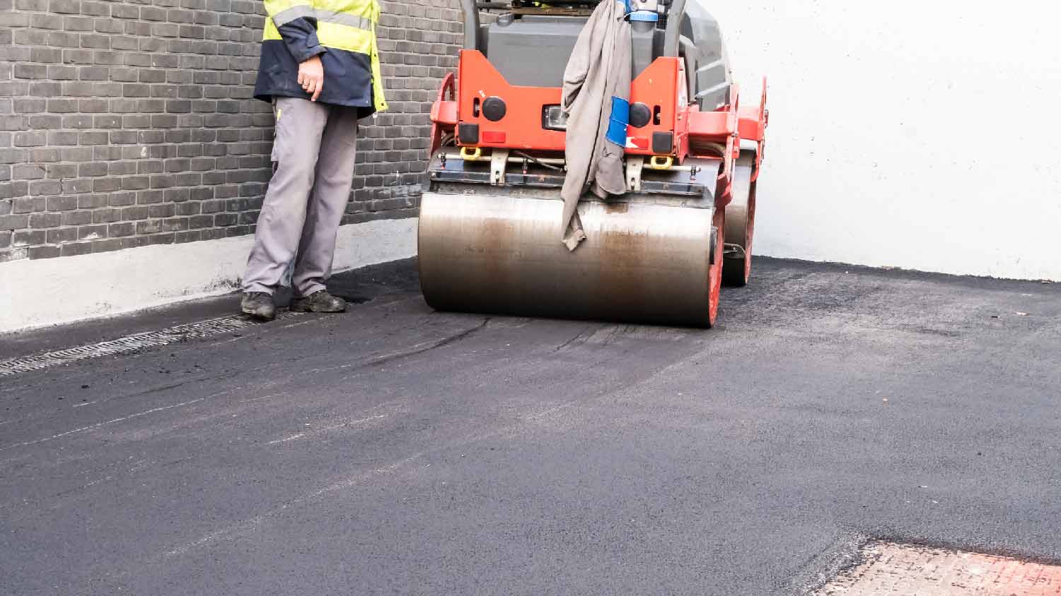 Workers smoothing an asphalt driveway with an asphalt roller