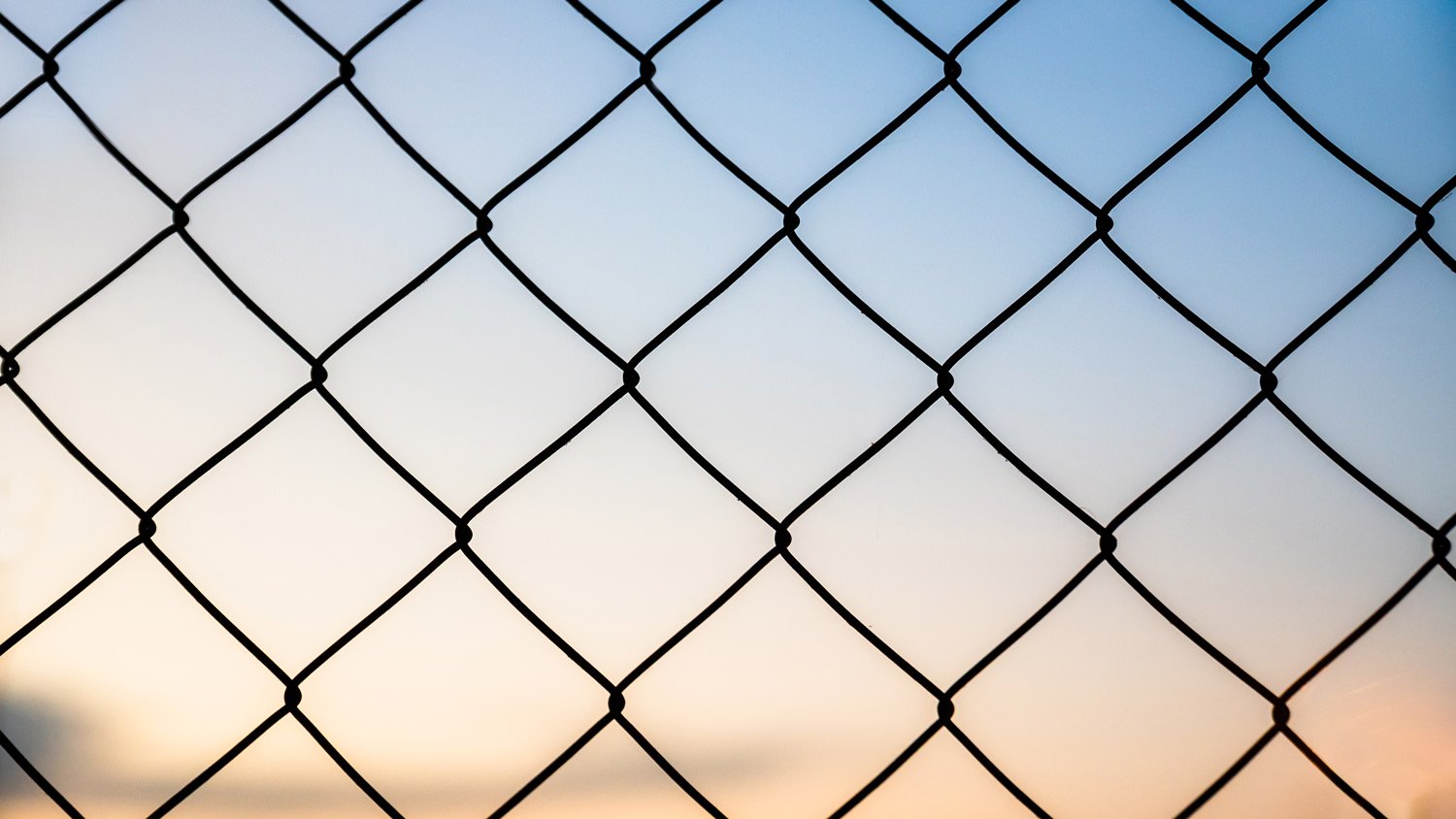 Close-up of a chain link fence with the sunset sky