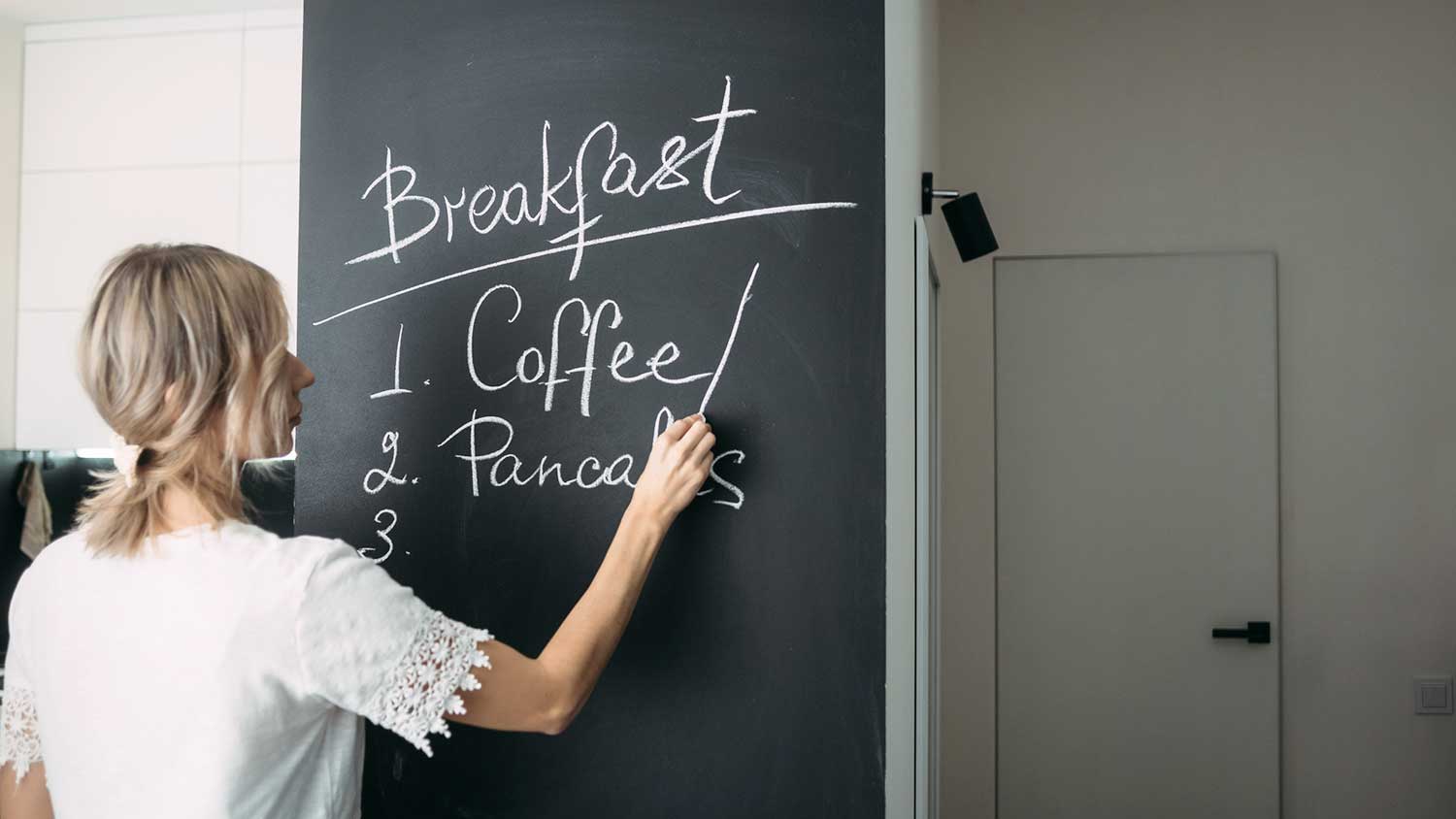 Woman using chalk to write on a black board wall