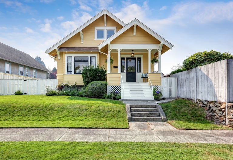 exterior of small house with yellow painted siding, green grass, and concrete sidewalk