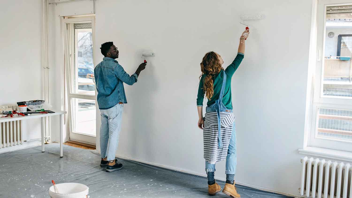 Young couple using paint rollers to paint an interior wall