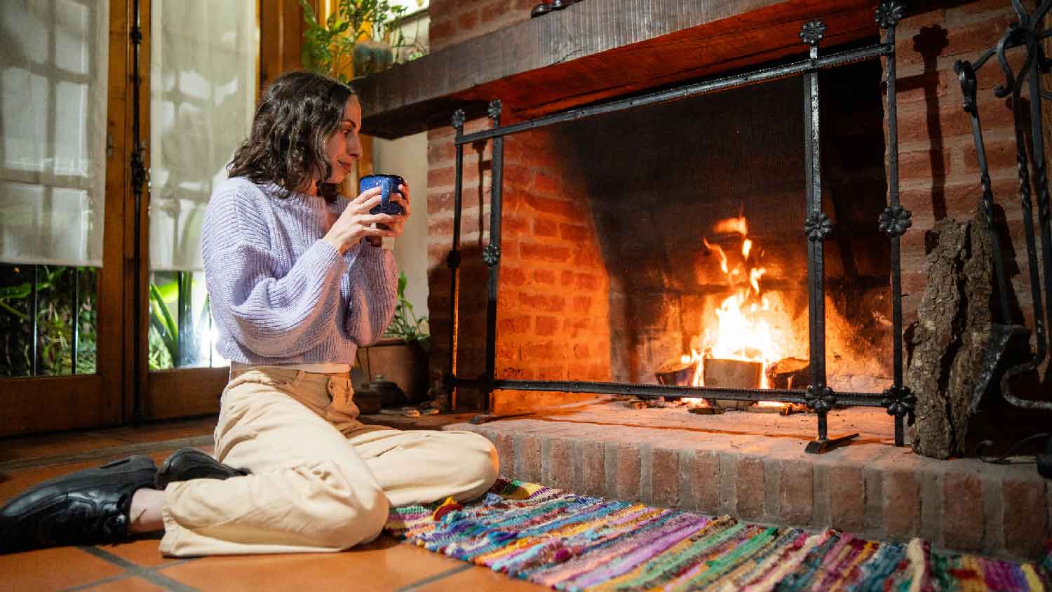 A young woman drinking a beverage in front of the fireplace