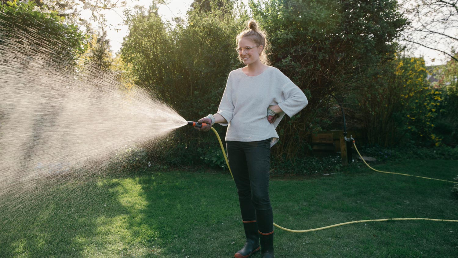 A young woman sprinkling the lawn in the garden