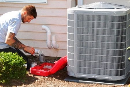 HVAC technician kneeling on ground while performing maintenance on a/c unit.