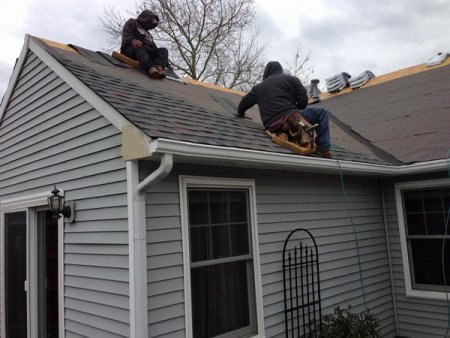 crew on roof replacing asphalt shingles during winter