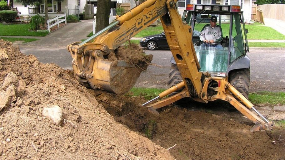 Backhoe excavating ground to dig up and replace damaged sewer pipe.
